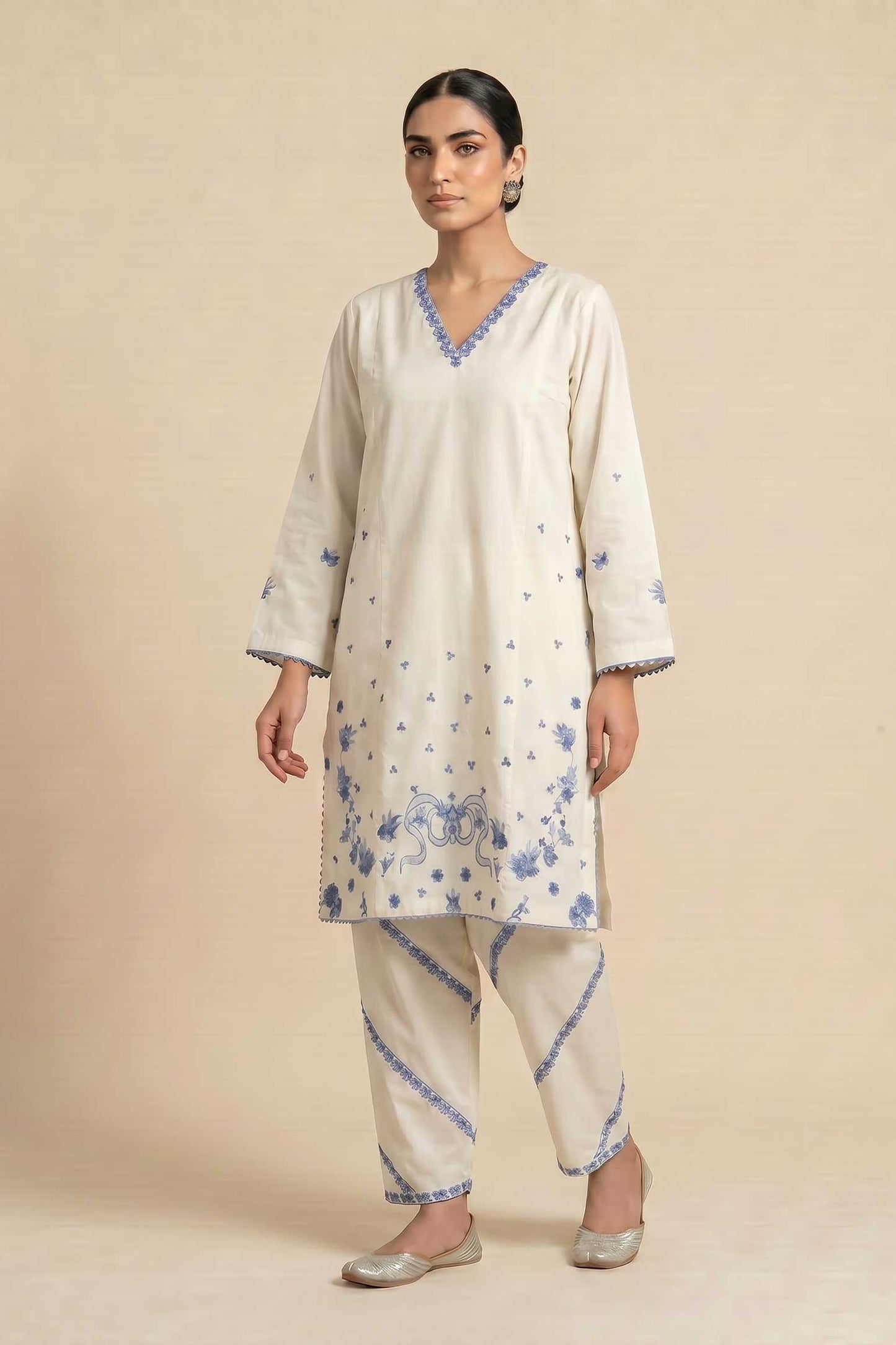 Woman wearing a cream-colored kurta with blue floral patterns on a beige background