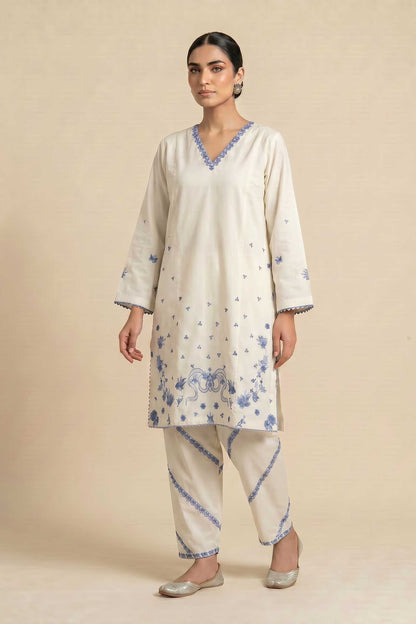 Woman wearing a cream-colored kurta with blue floral patterns on a beige background
